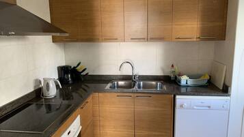 A compact kitchen with wooden cabinets, a stainless steel sink, a dishwasher, and a coffee maker.