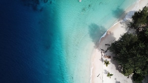 An aerial view of a beach with clear turquoise waters, white sand, and dense green foliage. - Ora Sunrise View Resort (Salemang)