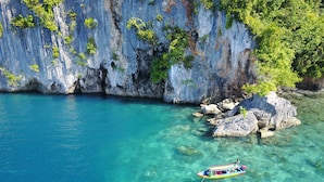 A boat anchored near a rocky coastline with clear turquoise water. - Ora Sunrise View Resort (Salemang)