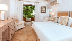 A hotel room with a large bed, a wooden nightstand, a desk, and a view of a tropical garden.
