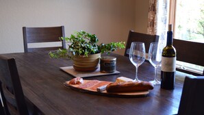 Une table de salle à manger en bois, agrémentée d’une plante en pot, d’une bouteille de vin et d’une planche de fromages accompagnée de charcuteries et de pain.