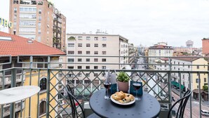 A balcony with a table set for two, featuring a plate of bread and a bottle of wine.