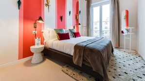 A bedroom with a bed, bedside table, lamp, and a view of the outside.