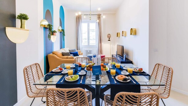 A dining area with a table set for breakfast, a sofa, and a TV in the background.