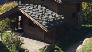 Una cabaña de madera con techo de piedra, con montañas al fondo.