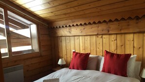 Una habitación de cabaña de madera con una cama, dos almohadas rojas, una lámpara blanca y una ventana.