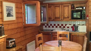 Una cocina con paneles de madera, una mesa redonda de madera y sillas, un microondas, un tostador y una tetera.