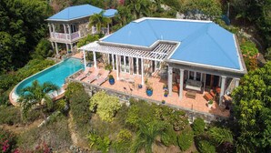 A large house with a swimming pool, a covered patio, and a lush garden. - Carnival Beach House Awaits: Relax in Style with Beachfront Views, A/C, and a Private Pool! (St John)