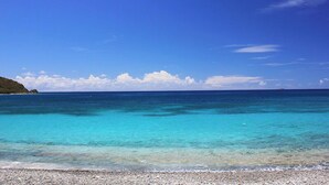 A clear blue sea with a pebbly beach and a distant landmass. - Carnival Beach House Awaits: Relax in Style with Beachfront Views, A/C, and a Private Pool! (St John)