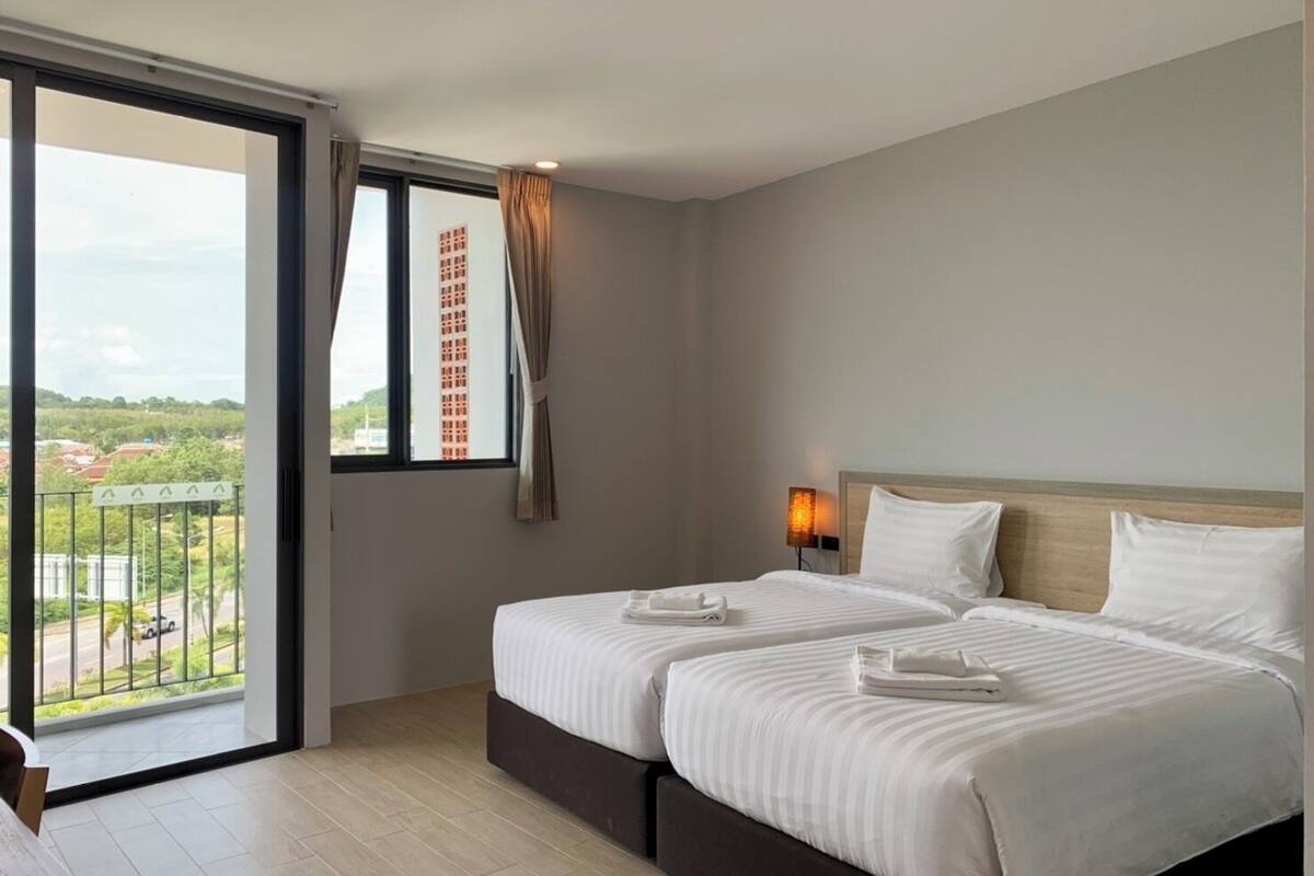 Una habitación de hotel con dos camas, un balcón con vistas y una mesita de noche con lámpara.