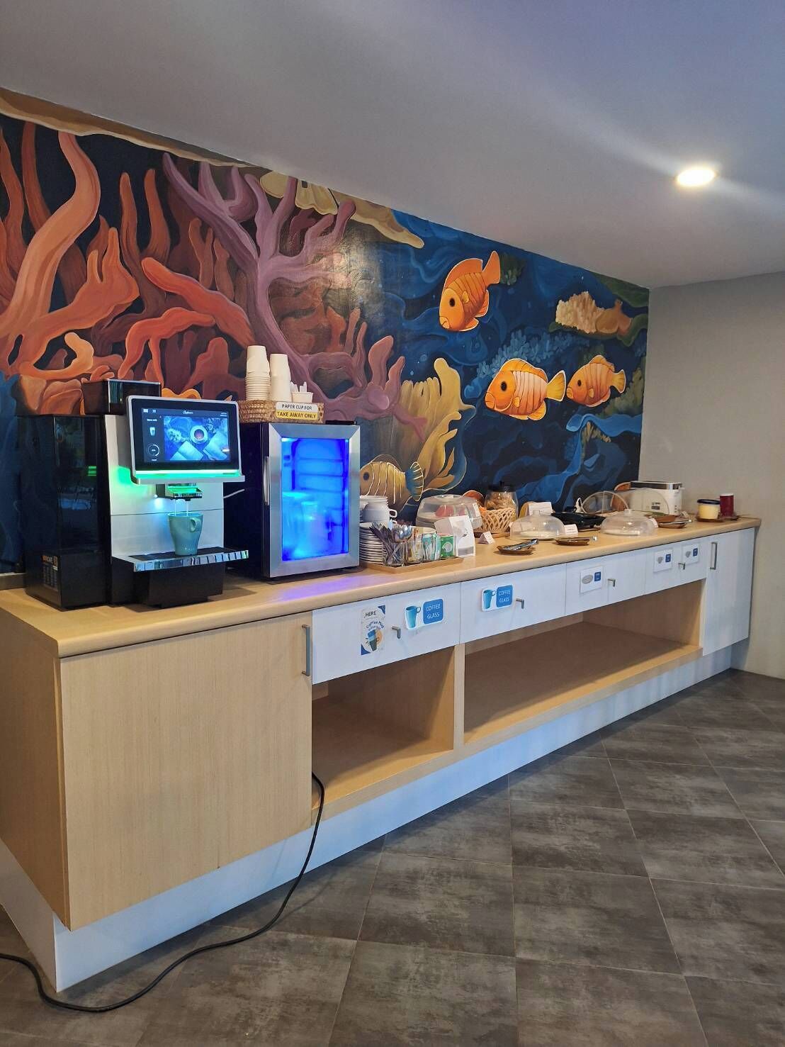 A counter with a coffee machine, a digital display, and a mural of fish and coral.