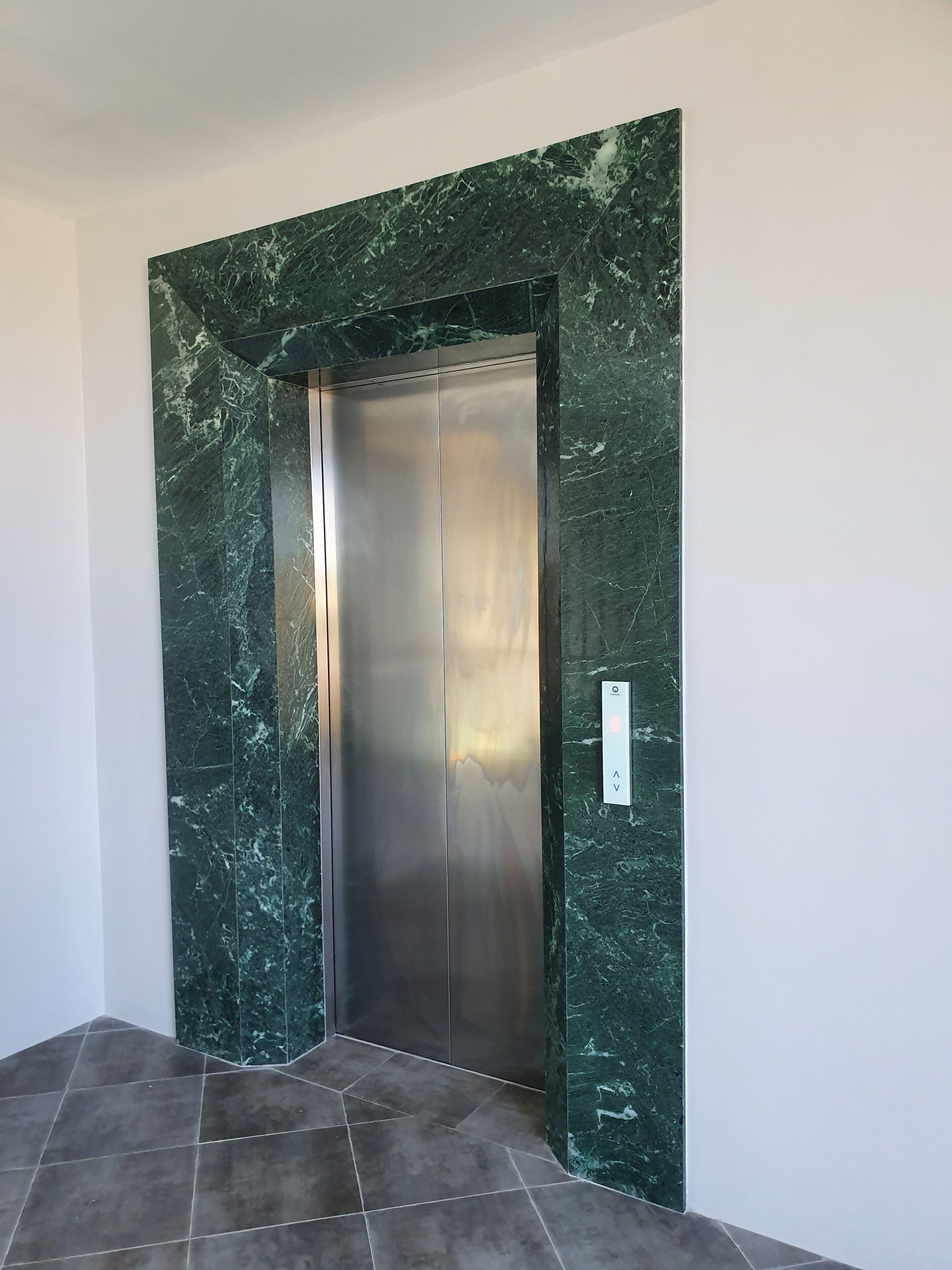 A modern elevator with a metallic finish and a green marble wall.