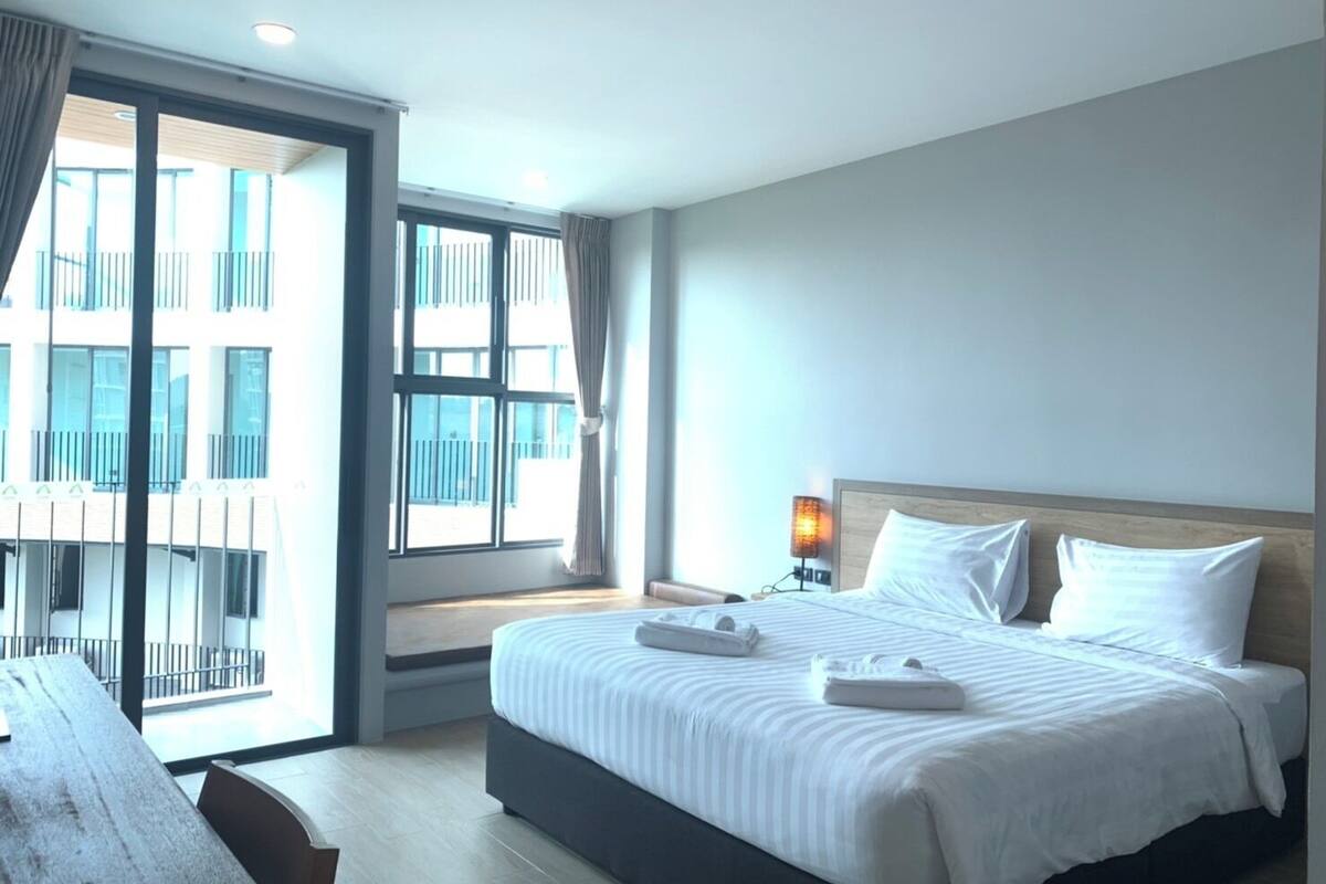 Habitación de hotel con una cama grande, un escritorio y vistas a un edificio a través de un ventanal.