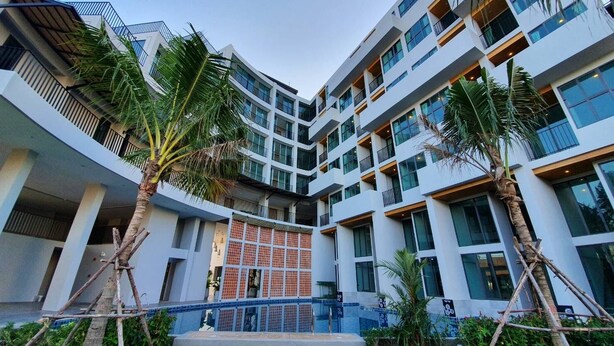 A modern multi-story building with a central courtyard, featuring palm trees and a tiled water feature. - Atom Phuket Hotel (Sa Khu)