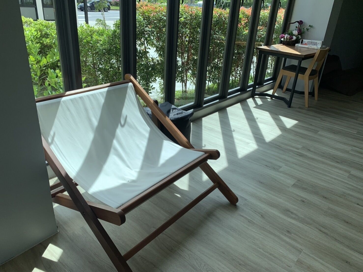 Un balcón con una silla y una mesa de madera, ventanas amplias y vistas al verdor.