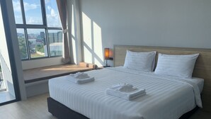 A hotel room with a large bed, a nightstand, a window with curtains, and a view of the city. - Atom Phuket Hotel (Sa Khu)