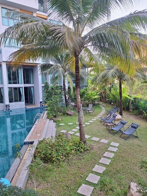 A poolside area with lounge chairs, palm trees, and a modern building with large windows. - Atom Phuket Hotel (Sa Khu)