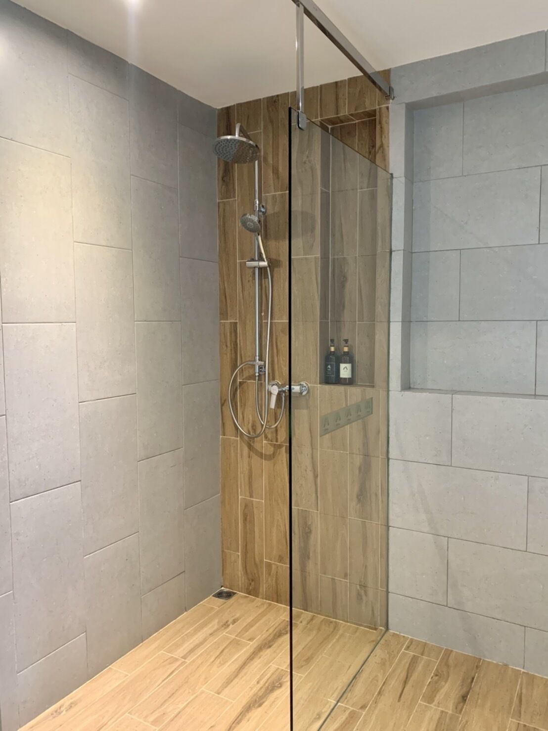 A modern shower area with a glass door, wooden paneling, and grey tiled walls.