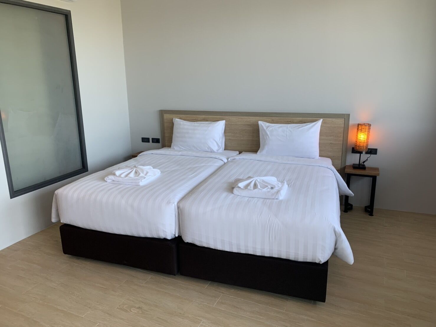 A double bed with white linens and two towels folded on the bed. There is a nightstand with a lamp to the right.