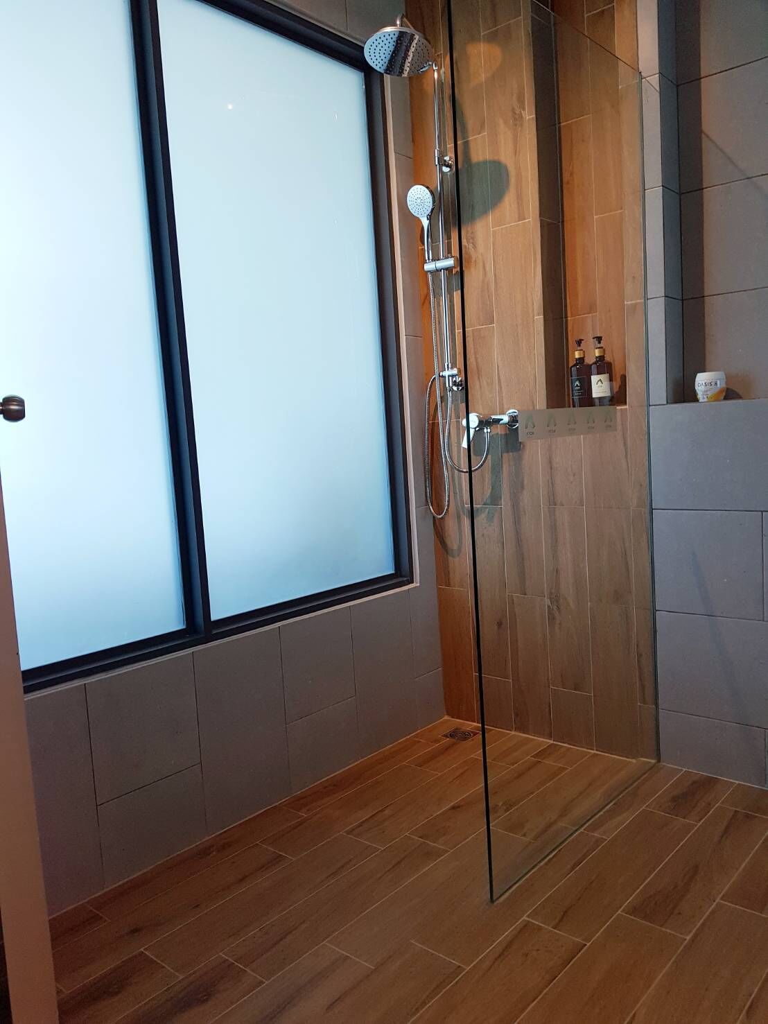 A modern shower with a glass door, wooden flooring, and a view of the outside.