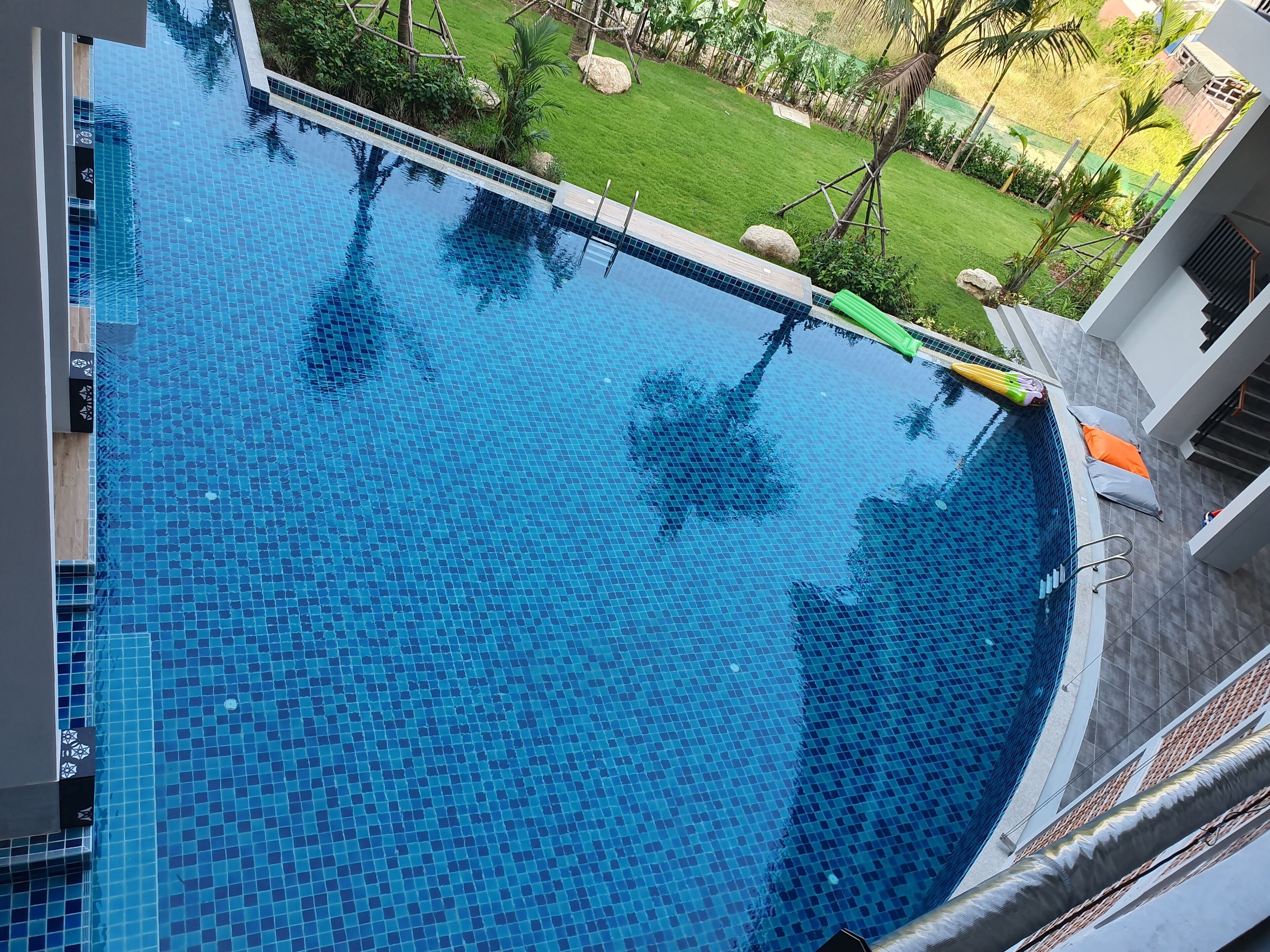 A large, clear blue pool with a tiled edge, surrounded by a well-maintained lawn and palm trees.