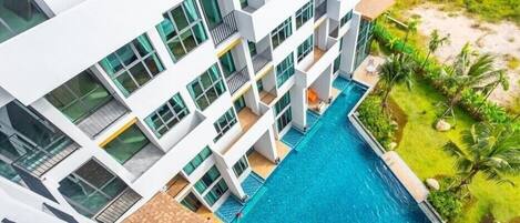Un hotel moderno con piscina central, varios balcones y un exuberante jardín.