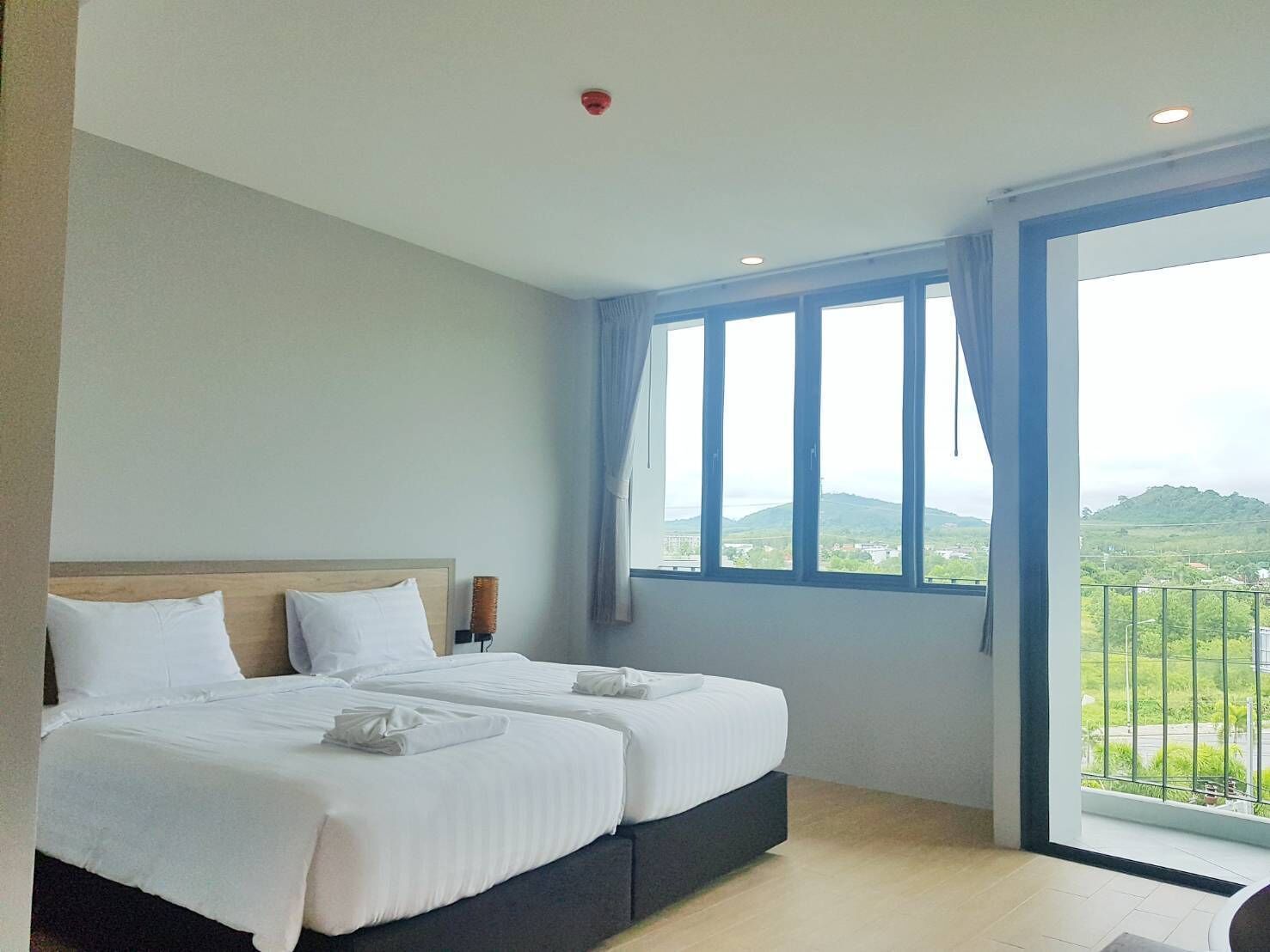 Une chambre d’hôtel avec deux lits, une grande fenêtre donnant sur la campagne et un luminaire au plafond.