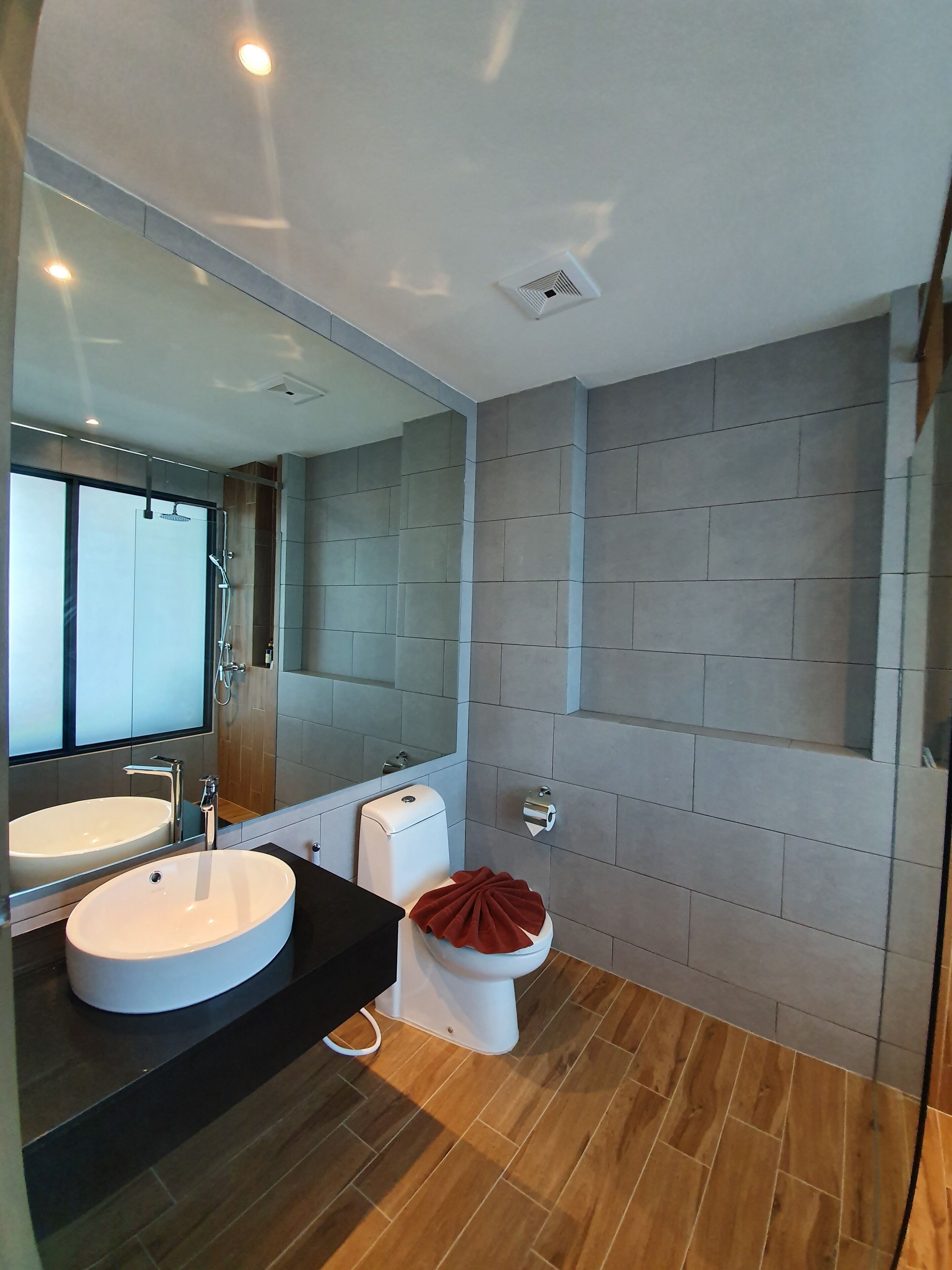 Un baño moderno con un espejo grande, un lavabo redondo, un inodoro y una ducha.