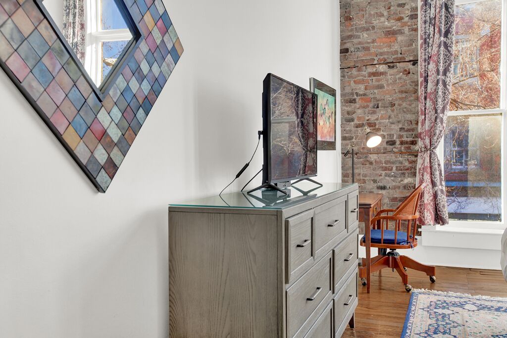 A room with a glass-top desk, a brick wall, a window with curtains, and a patterned rug.