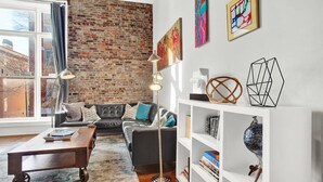 Ein Wohnzimmer mit Backsteinwand, einer Couch, einem Couchtisch, einer Stehlampe und einem Bücherregal.