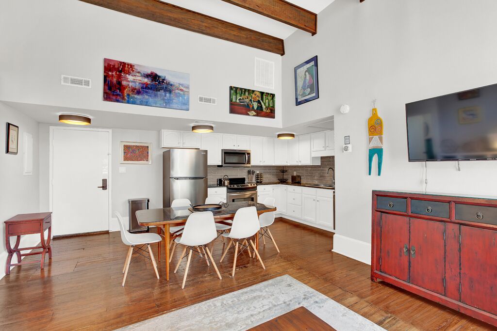 Une cuisine moderne avec des meubles blancs, des appareils en acier inoxydable et un coin repas comprenant une table en bois et des chaises blanches.