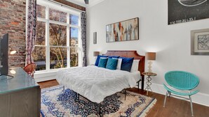 Ein Schlafzimmer mit großem Fenster, einem Bett mit blau-weißer Bettwäsche, einem Deckenventilator und einem blauen Sessel.