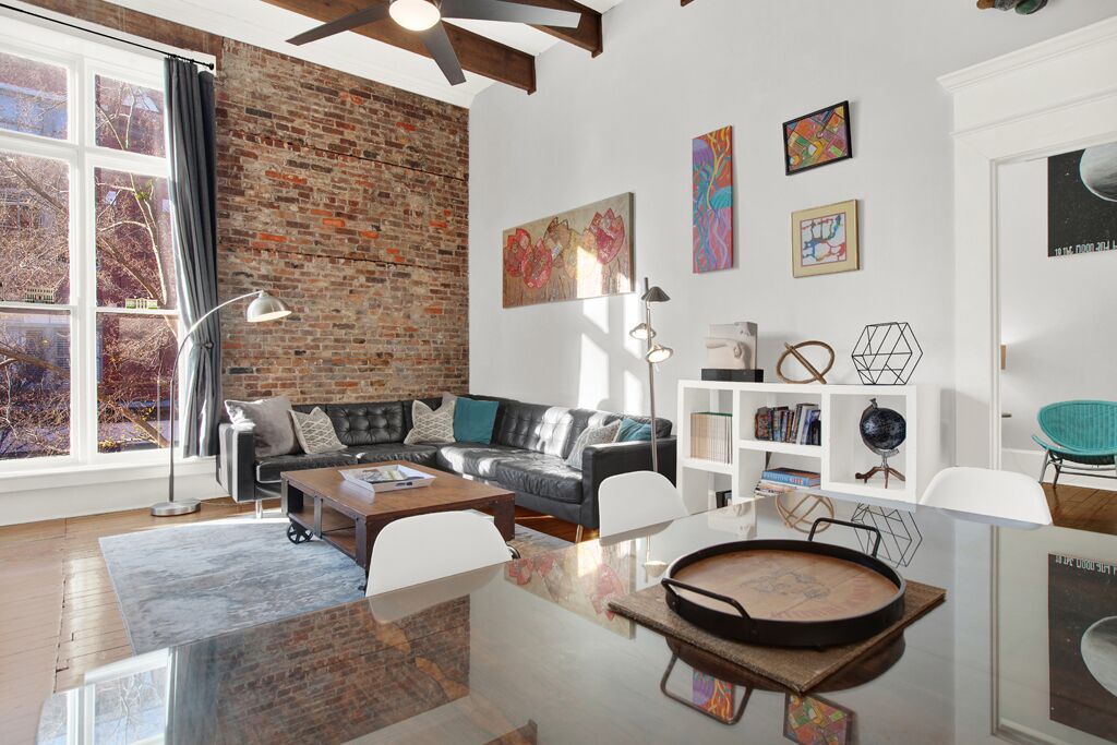 Un salon moderne avec un mur en briques, un canapé en cuir et une table à manger en verre.