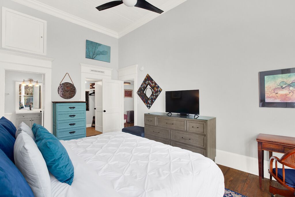 A bedroom with a large bed, a dresser, a television, and artwork on the walls.