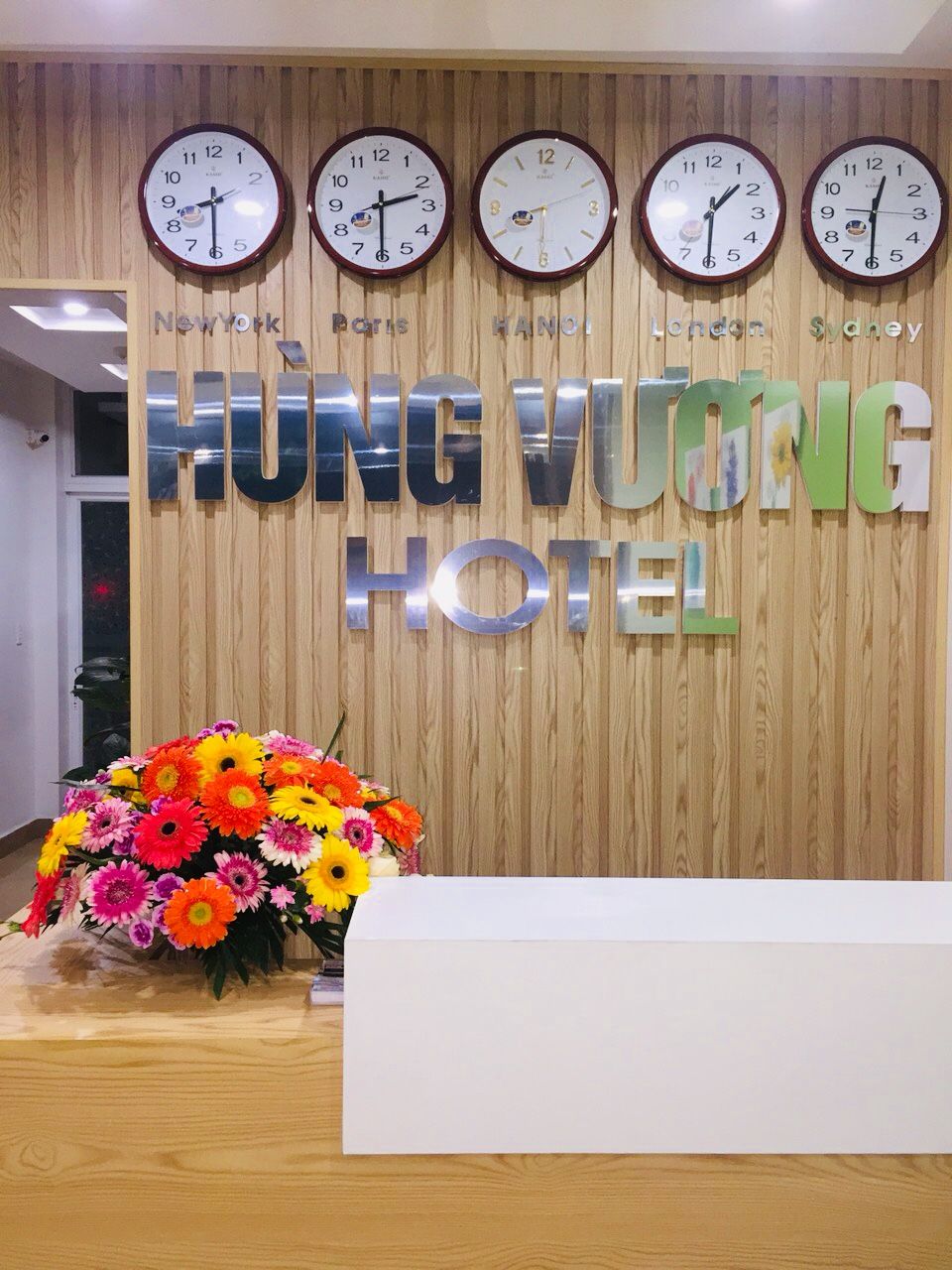 A reception desk with clocks displaying times for New York, Paris, Hanoi, London, and Sydney. The reception area has a wooden backdrop with the hotel name 'HUNG YUONG HOTEL' in large letters.