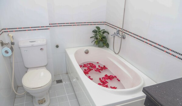 A bathroom with a toilet, a bathtub filled with rose petals, a shower, and a potted plant. - Hung Vuong Hotel (Hong Gai)