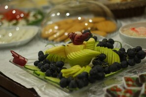 A buffet with sliced fruits and vegetables, including grapes, cucumbers, and apples, arranged on a tray.