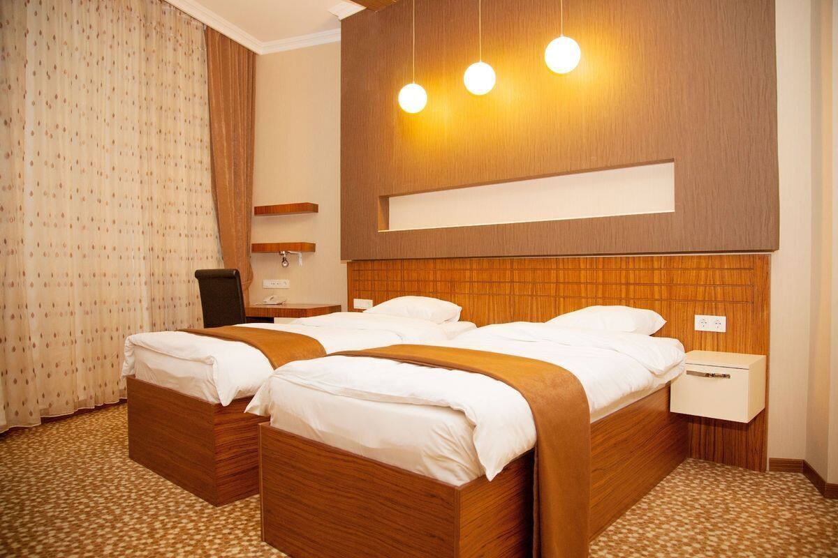 A hotel room with two wooden beds, a nightstand, a lamp, and a curtain.