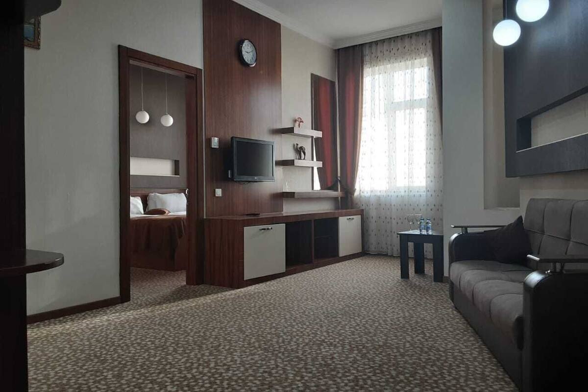 A hotel room with a bed, a TV, a small table, a sofa, and a carpeted floor.