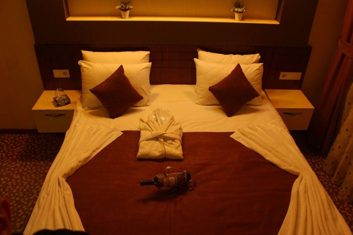 A hotel room with a neatly made bed, two pillows, a robe, and a small bottle on the nightstand.