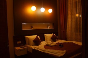 Habitación de hotel con una cama grande, una mesita de noche, un espejo sobre la cama y una ventana con cortinas.