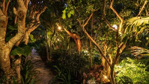 A stone pathway surrounded by lush greenery and trees, illuminated by soft lighting. - Villa Genevieve | Creole Elegance Above Gustavia (Lurín)
