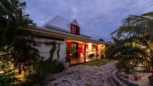A house with a white exterior, red shutters, and a stone pathway leading to the entrance. - Villa Genevieve | Creole Elegance Above Gustavia (Lurín)