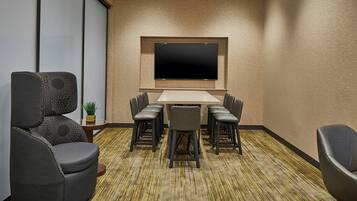 A conference room with a large flat-screen TV, a long table with six chairs, and a carpeted floor.