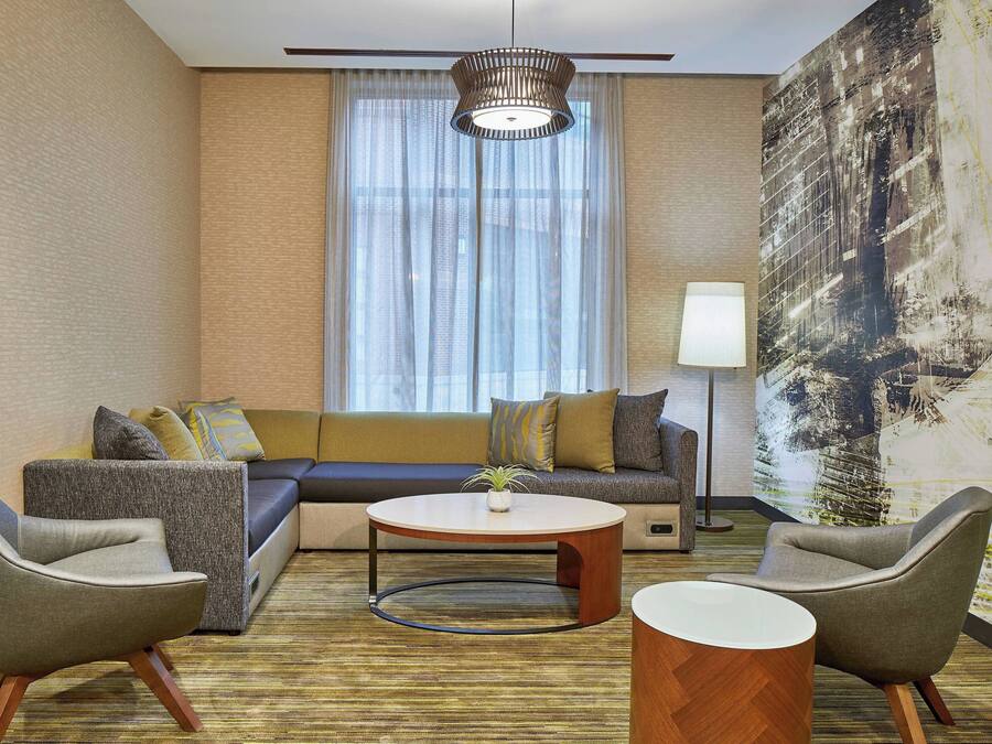 Una habitación de hotel moderna con un sofá modular, dos sillones, una mesa redonda y un cuadro abstracto grande en la pared.