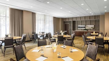 Un salón de conferencias de hotel con varias mesas redondas, sillas y una pantalla grande en la pared.
