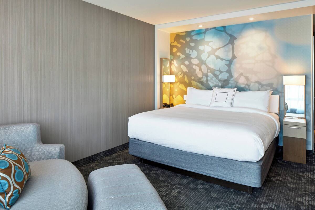 A modern hotel room with a large bed, a seating area, and a decorative wall mural.