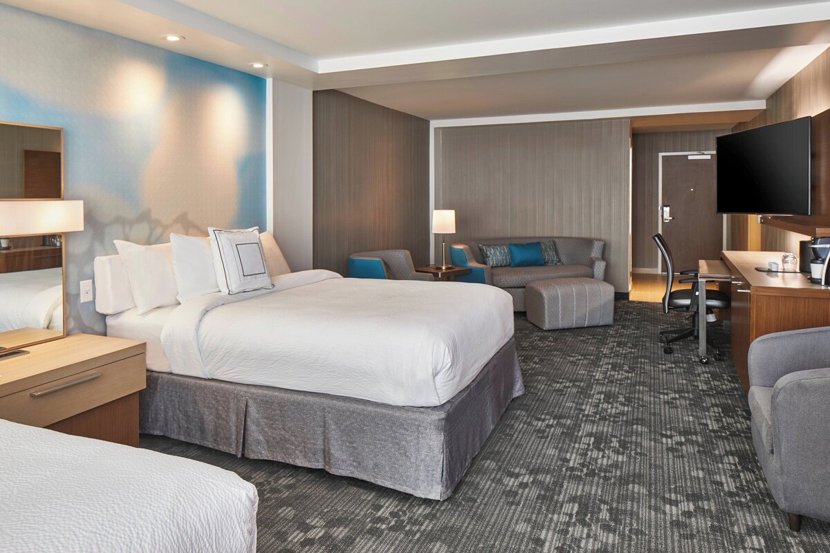 A hotel room with a large bed, a desk with a computer, a TV, and a seating area with a sofa and armchairs.