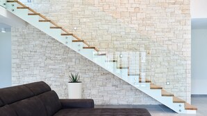 Un intérieur moderne avec un mur en pierre, un escalier en verre et un canapé de couleur sombre.