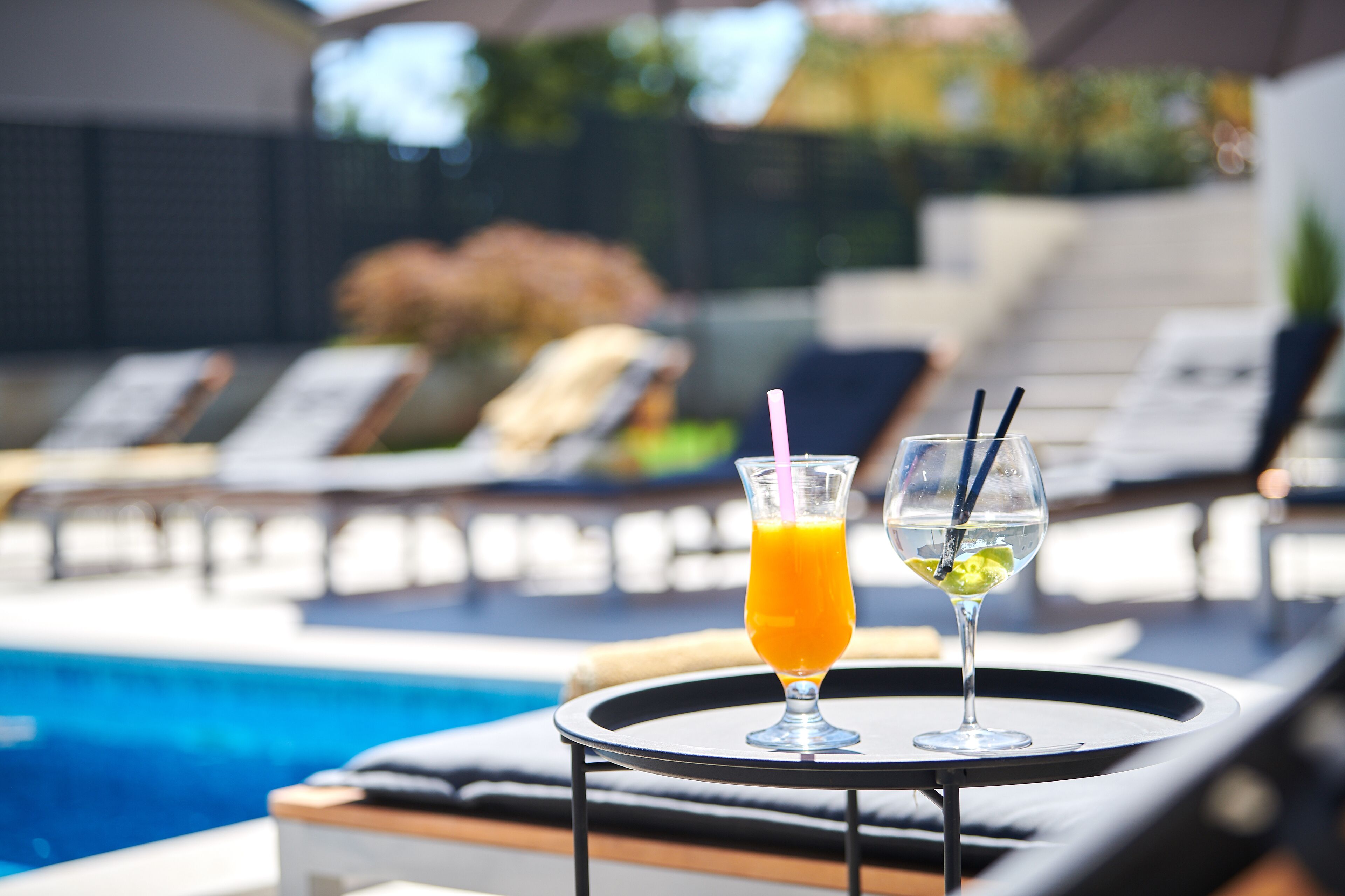 Un espace aménagé au bord de la piscine, avec des chaises longues et une table sur laquelle sont posées deux boissons.
